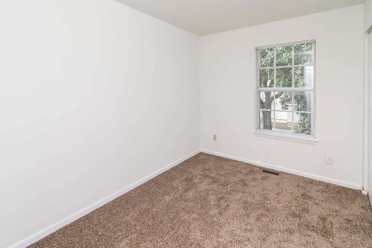 Hickory Hill Townhomes bedroom number 1 lookin in from doorway at the back wall with a large window. White walls and chocolate colored carpet