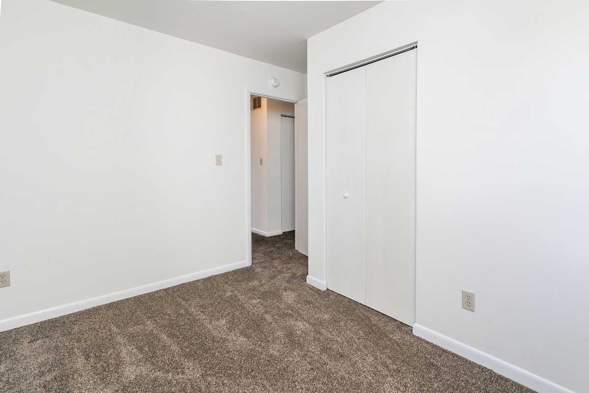 Hickory Hill Townhomes bedroom number 2 view of closet door, view out of door and into hallway. White walls, chocolate colored carpet