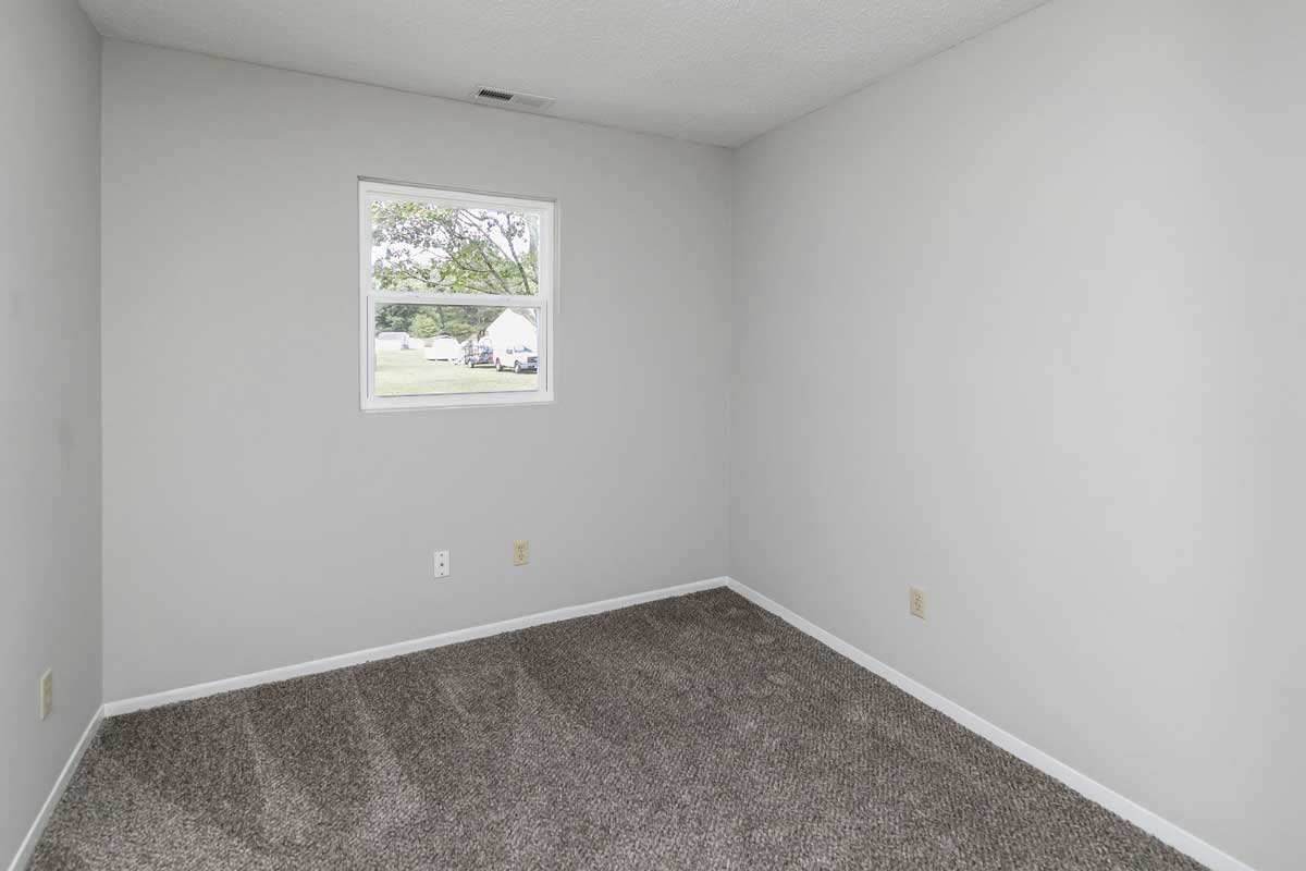 Township bedroom 1 view from door looking to back of room , window on back wall. Dark gray carpet; light gray walls with white trim