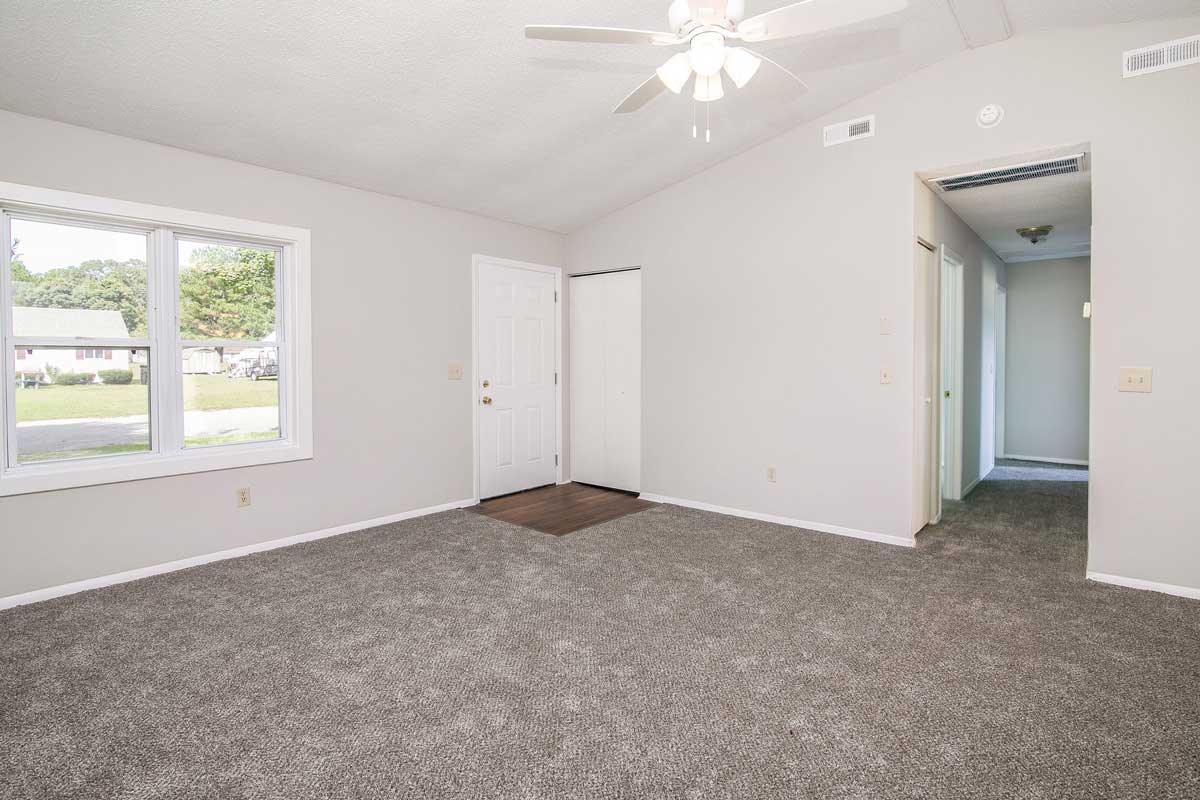 View from farthest corner of the living room, you can see the front window out to the street; front door which is closed and bifold doors to coat closet. Also view of hall way leading to bathroom and bedrooms.
