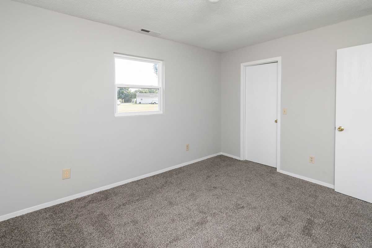 Township master bedroom view of window on back wall, door to walk in closet. Light gray painted walls, dark gray carpet