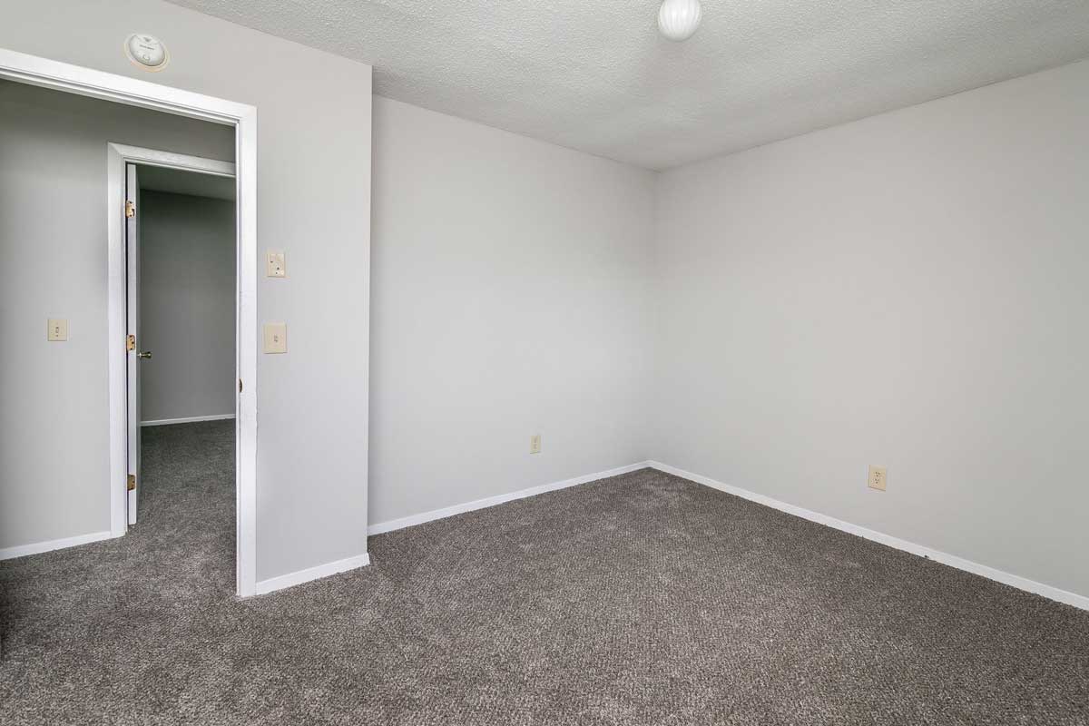 Township ranch style home master bedroom view from center of room showing doorway to hallway , then doorway to bedroom across hallway. Walls are light gray, carpet darker gray.